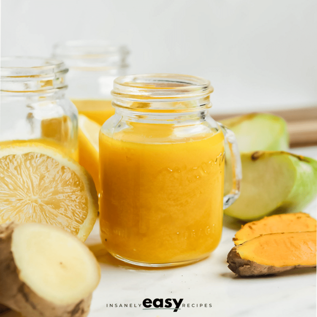 a small mason jar style shot glass with a handle, filled with blended ginger turmeric juice with fresh fruit around it