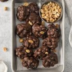 a sheet pan of peanut cluster candy with a small bowl of peanuts.
