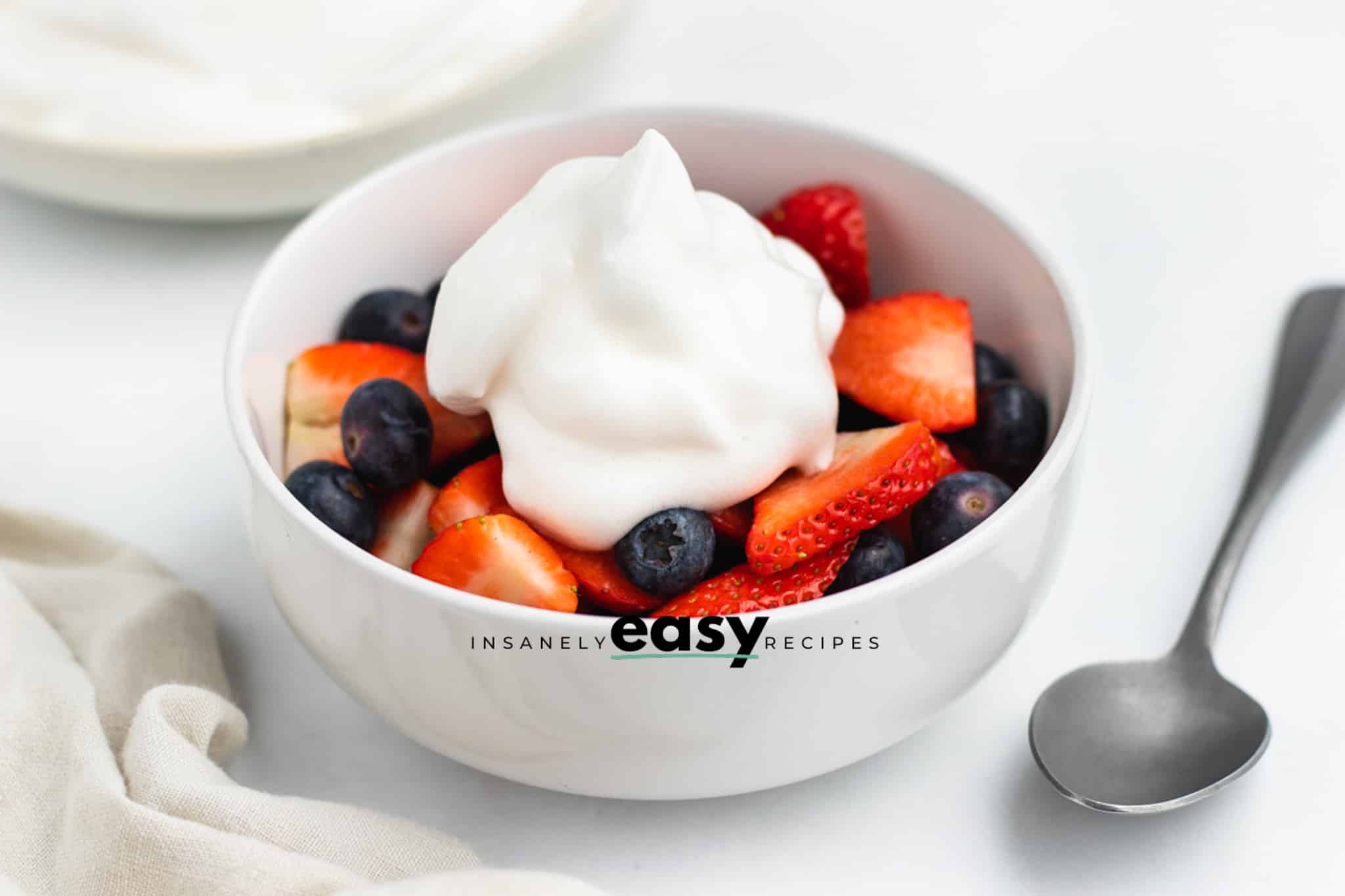 Photo of a bowl of chopped berries, like blueberries and strawberries, topped with a dollop of aquafaba whipped cream.