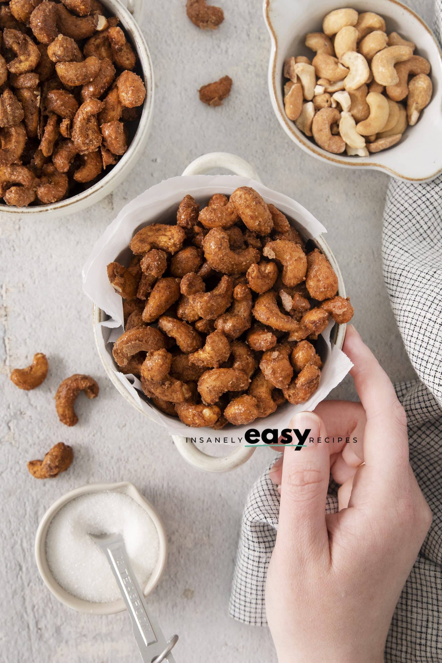 overhead view of bowls of candied cashews. A hand is reaching for them.
