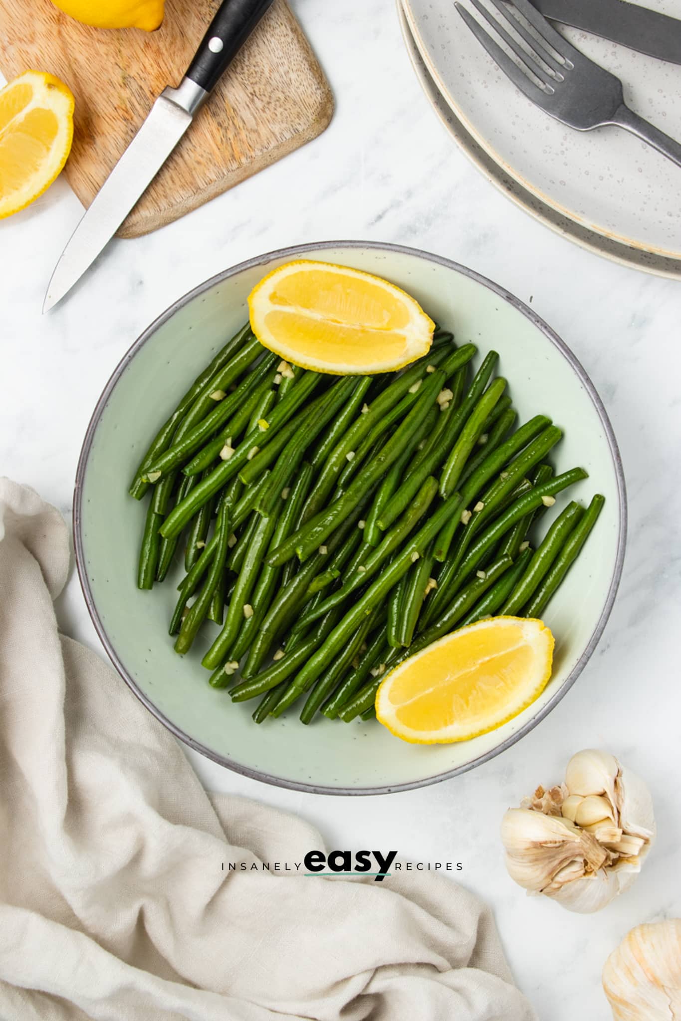 a serving bowl of sauteed green beans with garlic and two lemon wedges.