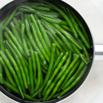 Uncut green beans boiling in a saucepan.