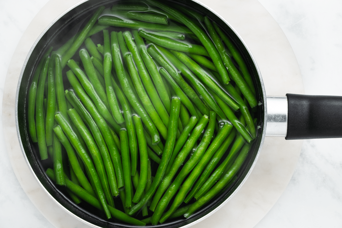 Uncut green beans boiling in a saucepan.