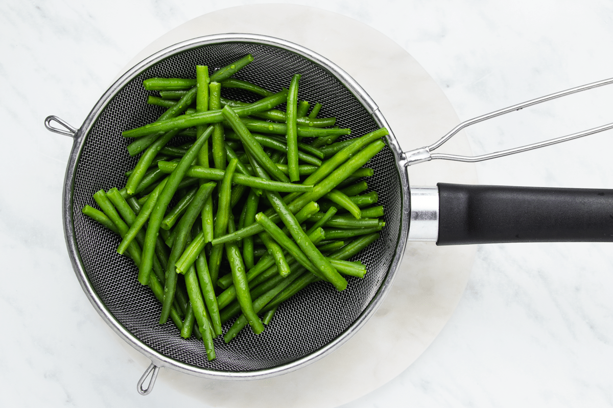Blanched green beans drained with a mesh colander.