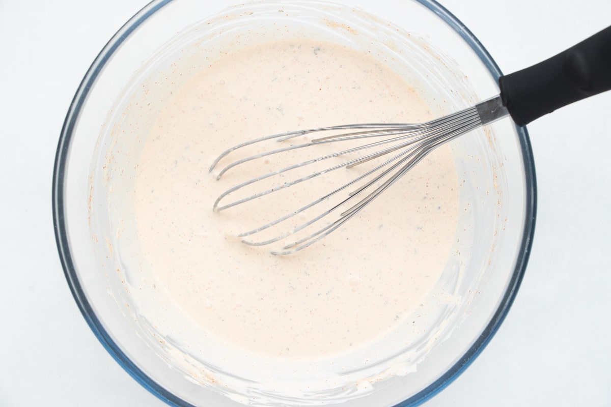 a whisk stirring seasoned sour cream in a glass bowl.