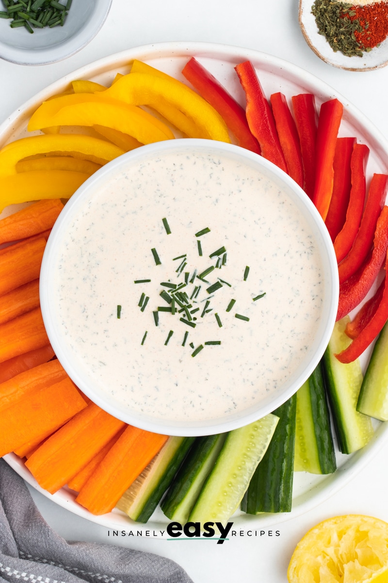 Top down view of a bowl of seasoned sour cream veggie dip, surrounded by colorful veggie crudite