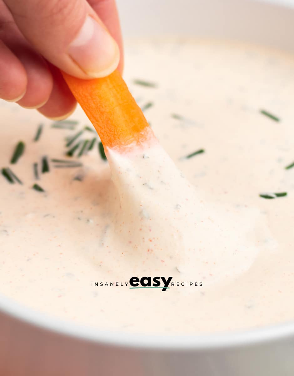 a person dipping a carrot by hand into a bowl of creamy seasoned sour cream